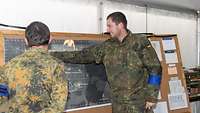 Ein Offizier weist einen Soldaten an eine Karte, die an einer Kartenwand befestigt ist, ein.