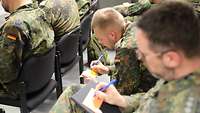 Soldaten in Uniform sitzen auf Stühlen und beschriften Zettel