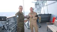 Zwei Soldaten in Uniform stehen an Deck und tauschen Geschenke als Erinnerungsgeste anlässlich des Besuches auf dem Schiff aus.