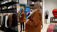 Eine Frau schaut in einen Spiegel und probiert eine Jacke mit Innenfell.