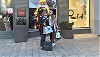 Zwei Frauen stehen mit mehreren Einkaufstaschen vor einem Einkaufsgeschäft.