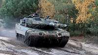 Ein Kampfpanzer Leopard 2 fährt über einen schlammigen Weg in Richtung des Sammelplatzes. 