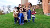 Mädchen und Jungen stehen, in historischen Gewändern am Fuße der Burganlage.