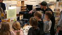 Eine Gruppe Kinder steht vor einem 3D-Drucker.