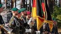 Mehrere Soldaten stehen als Fahnenabordnung mit zwei Fahnen nebeneinander in der Sonne. 