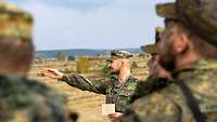 Ein Soldat zeigt anderen Soldaten, die um ihn herum stehen, etwas im Gelände.