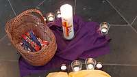 Eine Kerze und ein Korb mit Schokolade stehen auf einem lila Tuch