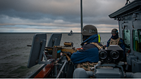 In der Nock einer Fregatte stehen zwei Soldaten in Gefechtsausrüstung am Maschinengewehr. Im Hintergrund ein weiteres Schiff.