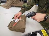 Ein Soldat scannt ein Etikett eines Bündels zusammengelegter Bundeswehr T-Shirts.