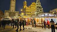 Beleuchtete Marktstände auf dem Weihnachtsmarkt, im Hintergrund stehen historische Gebäude.