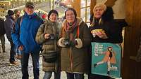 Vier Personen stehen mit Glühwein und Bratwurst für ein Gruppenbild zusammen.