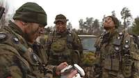 Drei Soldaten stehen um ein neues Bedienfeld für Drohnen herum, ein Soldat schaut in den Himmel. 