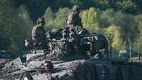 Zwei Soldaten in Schutzausrüstung sitzen auf einem Schützenpanzer Marder, im Hintergrund Laubwald.