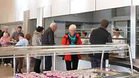 Mehrere Menschen mit Essenstablett in einer Kantine.