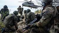 Soldaten warten an einem Waldrand während ein großer Hubschrauber zur Landung ansetzt.