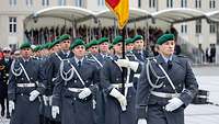 Soldaten im Dienstanzug marschieren auf einem Festplatz ein. Sie tragen eine Deutschlandflagge