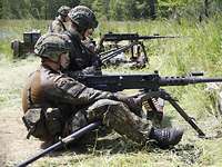 Soldaten im Kampfanzug sitzen an großen Waffen und üben mit diesen. Sie sind in der Natur.