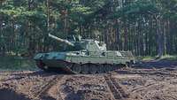 A tank is standing in an open area in front of a forest