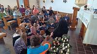 Kinder und Pfarrer sitzen vor den Adventskränzen bei einer Andacht in der Kapelle