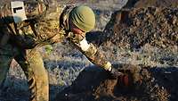 Ein Soldat zeigt einen Sprengsatz, der in einem Erdhaufen versteckt ist.