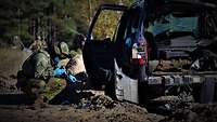 Ein Soldat fotografiert mit Handschuhen Wrackteile eines Autos in einem Gelände.