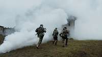 Drei Soldaten laufen auf ein Gebäude zu. Dieses ist in Nebel gehüllt.