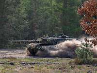 Ein Panzer fährt durch einen Wald und wirbel dabei Staub in die Luft.