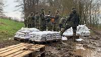 Auf Paletten liegen zahlreiche Sandsäcke, die von Soldaten in der Kette weitergereicht werden