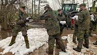 Soldaten reichen Sandsäcke in der Kette weiter. Am schlammigen Boden liegen zahlreiche Sandsäcke.