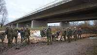 Mehrere Soldaten legen Sandsäcke vor einer Brücke aus 