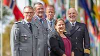 Vier Soldaten und eine Beamtin haben sich zum Gruppenfoto aufgestellt, im Hintergrund wehen Flaggen 