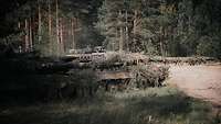 Ein Soldat schaut aus einem Kampfpanzer vom Typ Leopard 2. Um ihn herum befindet sich Wald.