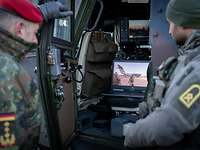 Zwei Soldaten schauen auf einen Laptop, der in einem Fahrzeug steht.