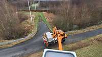 Ein orangener Lkw von der ausgefahrenen Hubbühne aus gesehen steht auf einem auslaufenden Feldweg