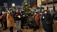 Mehrere Leute stehen vor einem Christbaum mit Glühweintassen. 