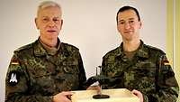 Zwei Soldaten halten ein Modell der Überwasserdrohne in einer flachen Holzkiste zwischen sich.