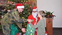 Ein Weihnachtsmann und ein Soldat mit Weihnachtsmütze übergeben einem Jungen sein Geschenk.