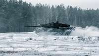 Ein Kampfpanzer fährt mit hoher Geschwindigkeit über den schneebedeckten Boden auf einem Übungsplatz in Litauen.