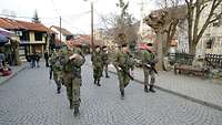 Mehrere Soldaten laufen bewaffnet eine Straße entlang.