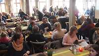 Menschen sitzen an Tischen in der Festscheune von Karls Erdbeerdorf.
