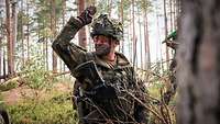 Ein Soldat gibt in einem Wald Kommandos mit Handzeichen. 