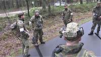 Mehrere Soldaten stehen auf einer asphaltierten Waldstraße im Halbkreis.