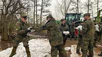 Mehrere Soldaten stapeln Sandsäcke an einem Flussausläufer.