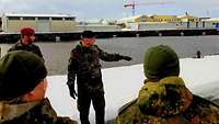 Ein Oberst steht mit Soldaten an einer schneebedeckten Pier