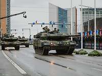 Mehrere deutsche Panzer fahren durch eine Stadt, litausche Soldaten salutieren am Straßenrand.