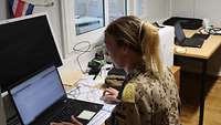 Eine Soldatin in Uniform sitzt im Büro an ihrem Arbeitsplatz. Dort stehen Computer.