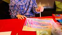 Ein Kind bemalt ein Bild mit bunten Wasserfarben.