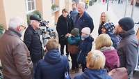 Eine Menschgruppe steht bei einer Stadtführung auf dem Marktplatz in Schwerin beisammen. 