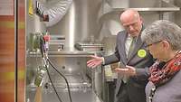 A man shows the equipment in a small kitchen to a woman.