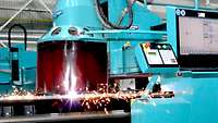 A turquoise gadget in a big factory hall starts welding.